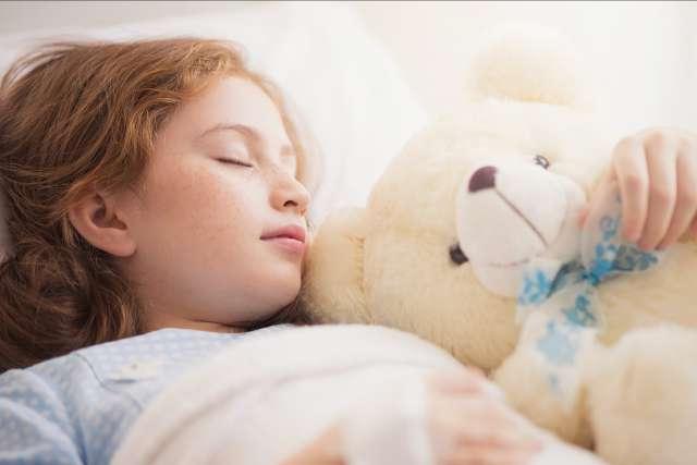 可爱的小女孩和她的泰迪熊躺在医院的病床上.