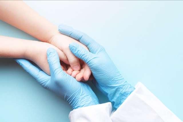 Doctor's hands in gloves holding child's hands.