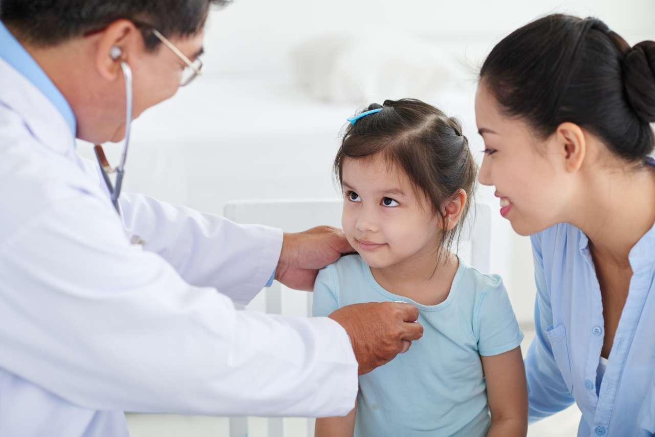 Doctor looking at his little patient while examining her with stethoscope.